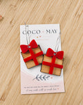 Christmas present earrings featuring golden gift boxes with bright red bows hanging from gold-tone hoops, displayed on a Coco & May earring card