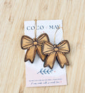 Natural bamboo bow-shaped dangle earrings with engraved detailing and dark outlines, displayed on a Coco & May jewellery card