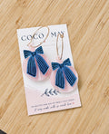 Navy and pink striped bow earrings hanging from gold-tone hoops, displayed on a Coco & May earring gift card