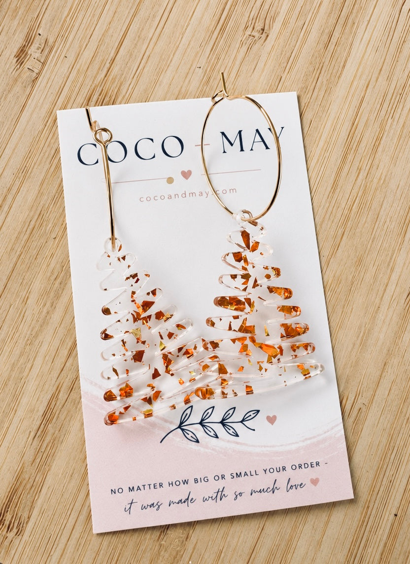 Clear acrylic Christmas tree dangle earrings with chunky gold acrylic details, displayed on a Coco & May jewellery card