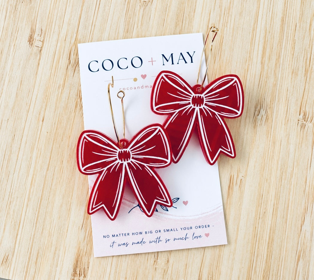 Red and white statement bow dangle earrings with contrasting decorative outlines, displayed on a Coco & May jewellery card