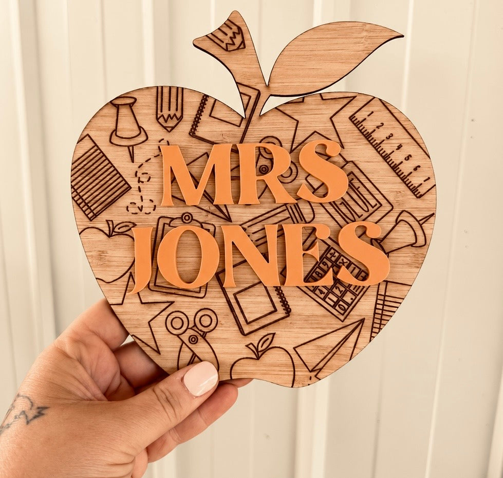 Personalised wooden apple-shaped classroom sign engraved with Mrs Jones and school-themed illustrations, handmade by Coco & May