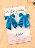 Bright blue and black striped bow earrings with gold-tone hoop fittings, displayed on a Coco & May jewellery card