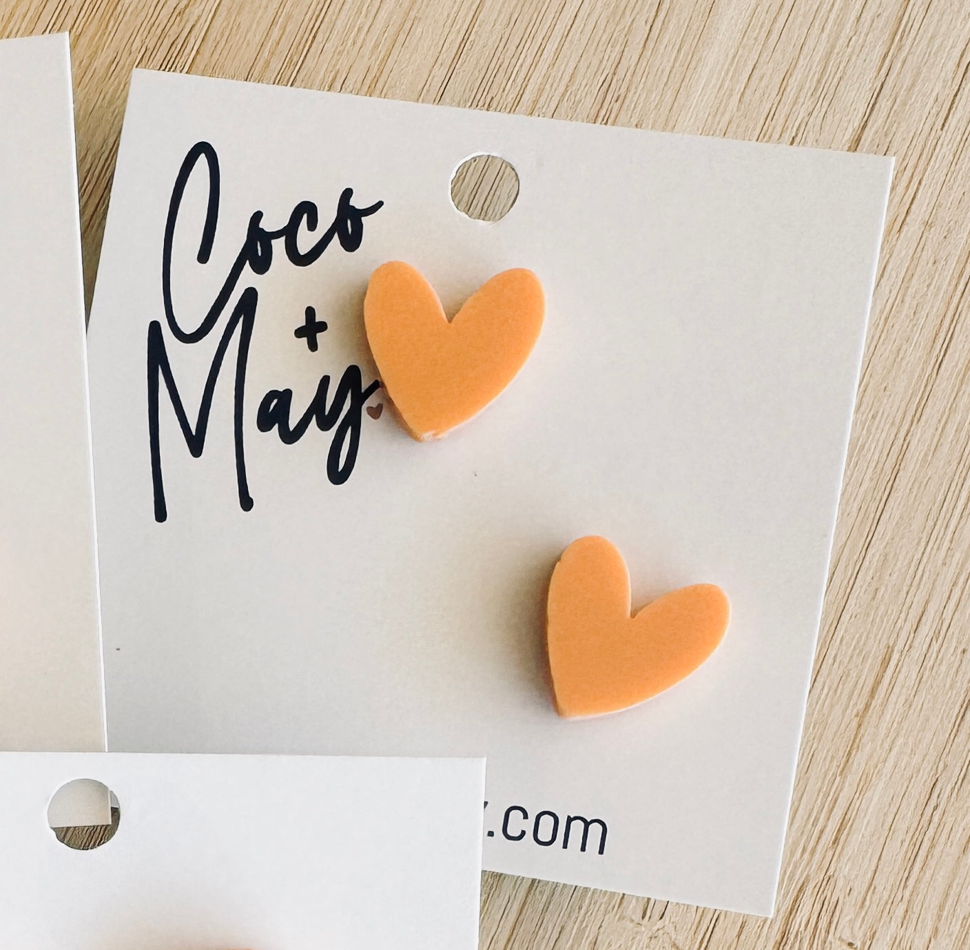 Orange acrylic heart earrings with marbled white pattern and gold glitter detail, displayed on a white Coco & May backing card.